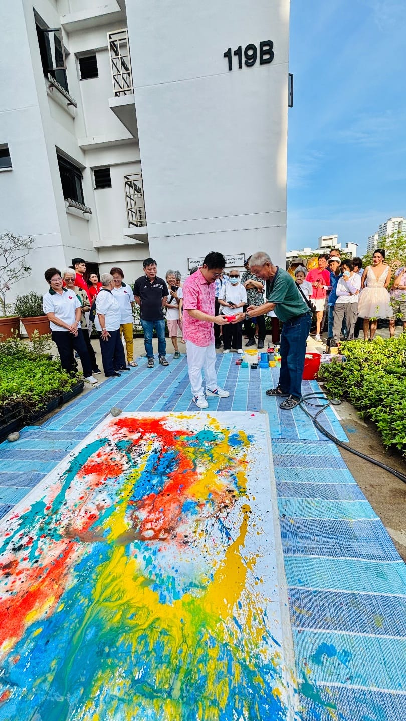Photo of a large paint splash artwork on the floor on top of plastic tarp and people watching in the background
